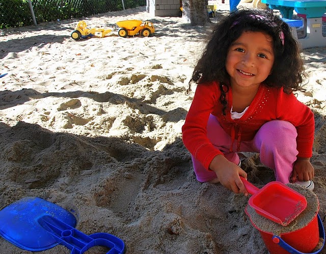 Smiling child playing in large sandbox.