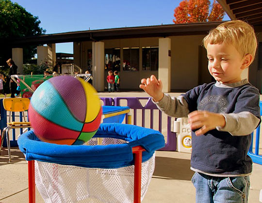 Preschool child shooting a basketball through a hoop.